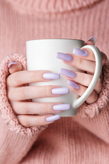 Girl's hands with delicate purple manicure holding a cup of tea.