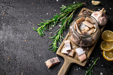 Salted herring in a jar on a cutting board with rosemary and lemon. 