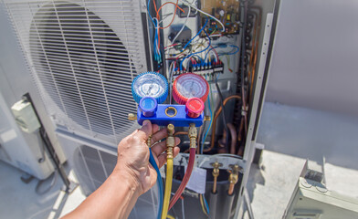 Air conditioning, HVAC service technician using gauges to check refrigerant and add refrigerant.