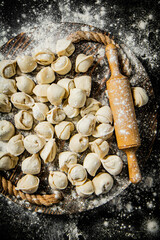 Raw dumplings on a wooden tray with a rolling pin and flour. 