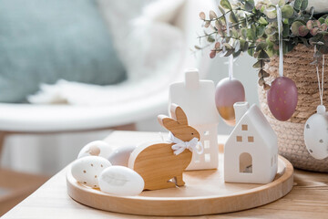 A beautiful postcard. The concept of the Bright Easter holiday. Flowers, rabbits, Easter eggs and Scandinavian white houses on a wooden table in a cozy living room.
