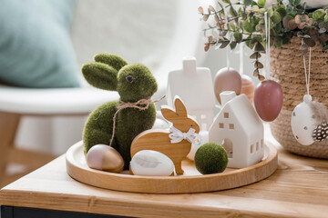 A beautiful postcard. The concept of the Bright Easter holiday. Flowers, rabbits, Easter eggs and Scandinavian white houses on a wooden table in a cozy living room.