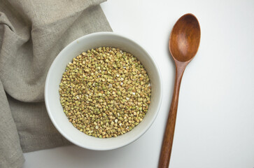green buckwheat in a white plate with a wooden spoon. the concept of proper healthy nutrition