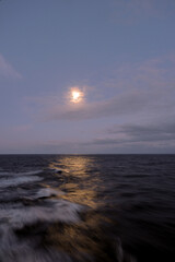 Obraz premium Full moon reflection on stormy rocky Atlantic Ocean during night seen from luxury ocean liner cruiseship cruise ship during transatlantic passage voyage 