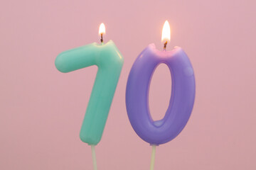 Burning birthday candles on pink background, number 70