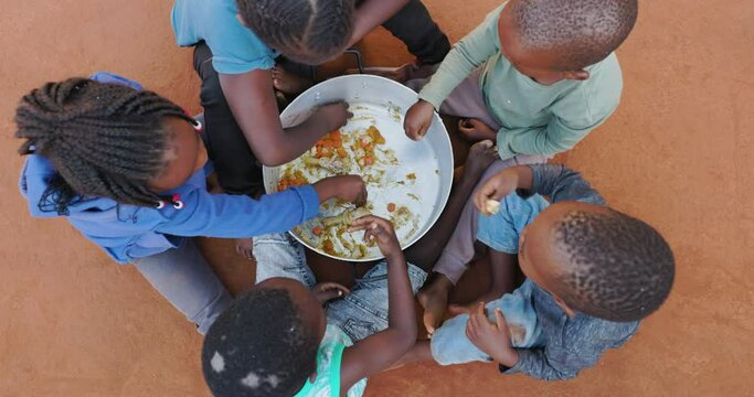 Poverty in Africa. Hungry Black African children scraping remains of food from the bottom of a communal cooking pot