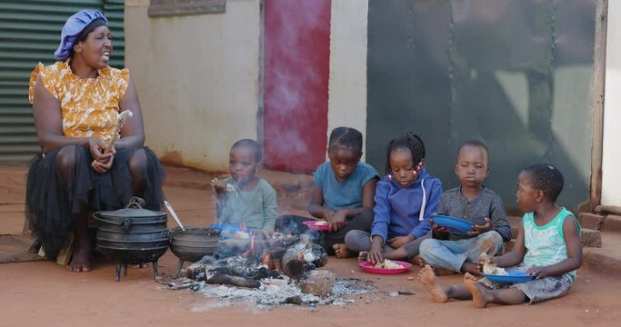 Poverty in Africa. Hungry Black African children sitting around a fire eating corn/maize and chicken