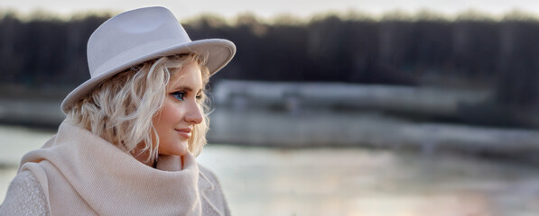 A beautiful woman in winter in a hat admires the landscape with a forest and a river. Only...