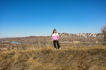 A teenage girl walks through the mountains. Happy young girl in a jacket in the wind. A walk in the fresh air.