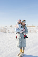 A pregnant young woman holds her daughter in her arms, standing in nature in winter