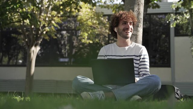 Male University student freelancer using laptop sitting on grass at Campus city park