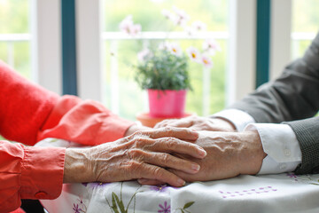Ein älteres Ehepaar hält sich an seinen Händen im Altenheim.
