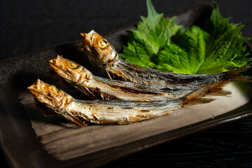 Grilled urume sardines on a black table. A side dish of sake.