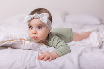 a girl with beautiful big eyes is rubbing the baby at home on the bed in a cotton bodysuit on white bed linen