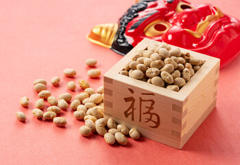 Beans for bean-throwing and masks of ogres placed on a background of red Japanese paper. Japanese ogres.
