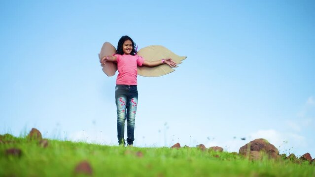 happy excited girl child with wings dancing like a bird on top hill in green meadow against blue sky - concept of freedom, aspirations and imagination