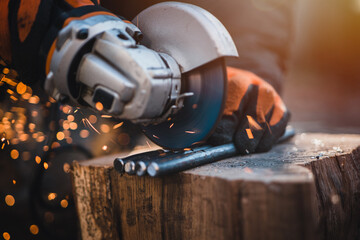 The hands of the master saw the metal with a grinder. Metal works in the workshop close up. Metal processing with angle grinder. Sparks in metalworking.