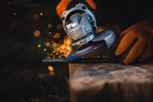 The hands of the master saw the metal with a grinder. Metal works in the workshop close up. Metal processing with angle grinder. Sparks in metalworking.