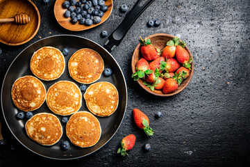 Pancakes in a frying pan with fresh berries and honey. 