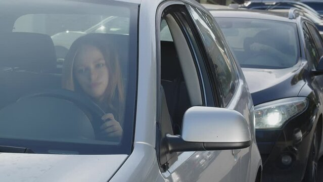 Stressed young woman sitting in her car in traffic jam. Impatient female driver expressing negative emotion. Rush hour concept. Annoyed girl in auto is running late