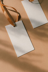 Closeup of blank label tags on beige background with shadows. Label hang tag design, hang tags clothing, swing tag design.