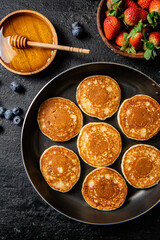 Pancakes in a frying pan with fresh berries and honey. 
