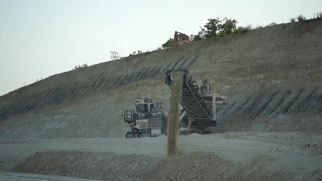 Earth mover cleans up soil for road renewal. Heavy duty mining machine at work. Quarry harvester unit with heavy equipment. Road constraction, repairing. Slow motion