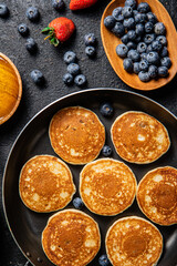 Pancakes in a frying pan with fresh berries and honey. 