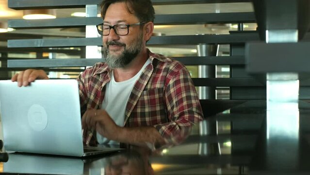 One young mature man with beard and eyeglasses working on a laptop on the table. People enjoy and use technology with computer and internet connection. Alternative workplace for modern adult male