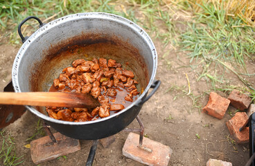 Cooking in an old cast iron cauldron on wood fire in the middle of nature. Traditional tasty way to cook in campfire.