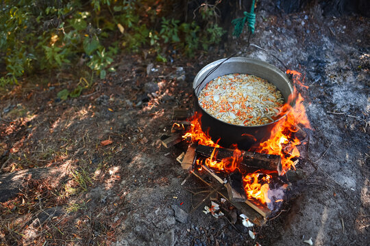 Cooking in an old cast iron cauldron on wood fire in the middle of nature. Traditional tasty way to cook in campfire.