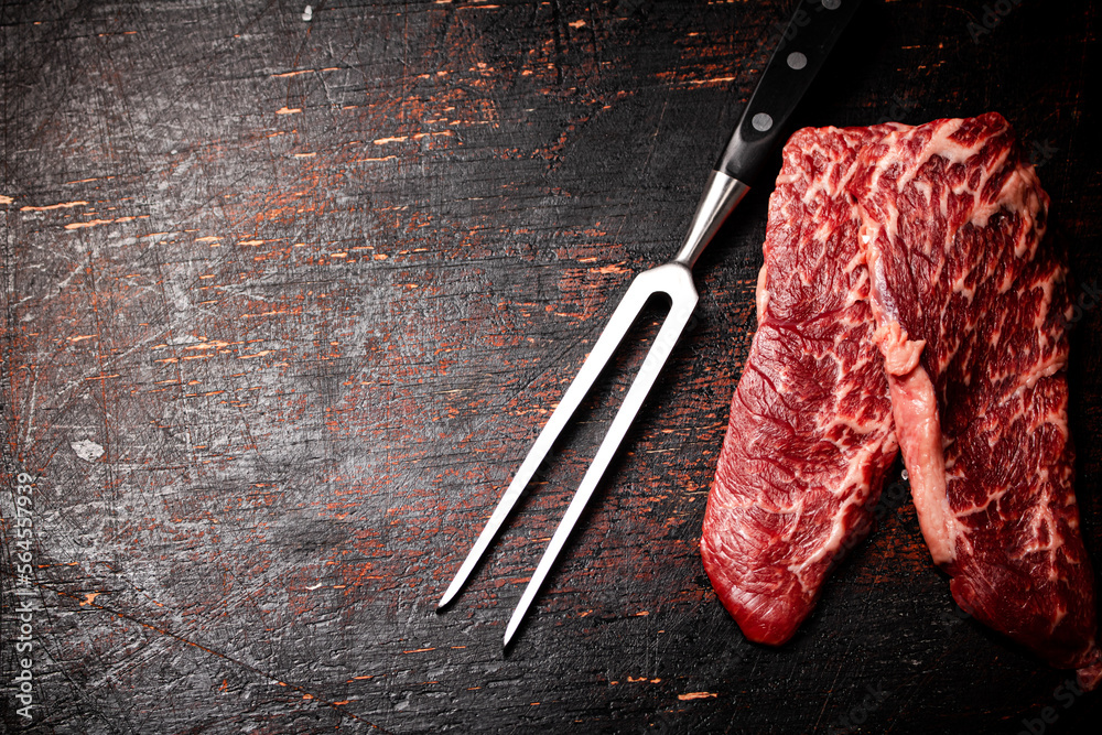 Poster Raw steak with a large fork on the table. 