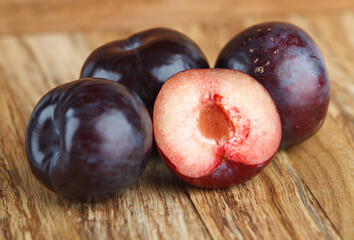 Obraz premium Dark blue plums isolated a wooden background. Fresh fruit whole and sliced. Fresh fruits.