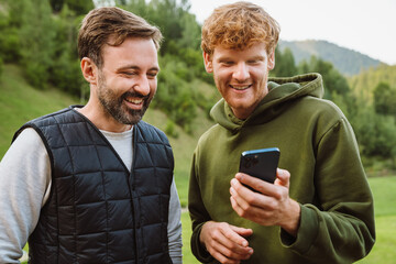 Two cheerful male friends using mobile phone while spending time in mountains