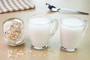 Oat milk in glass cups with dry oats in a bowl.