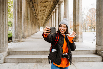 Excited asian woman tourist taking selfie and waving during walk through the old city street