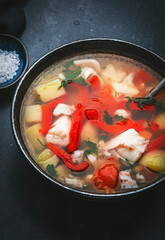 Fish soup with cod, paprika, potatoes, tomatoes and parsley in ceramic soup bowl on dark table background, top view