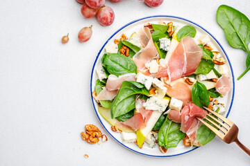 Fresh pear salad with jamon, blue cheese, spinach and nuts on white table background, top view, copy space