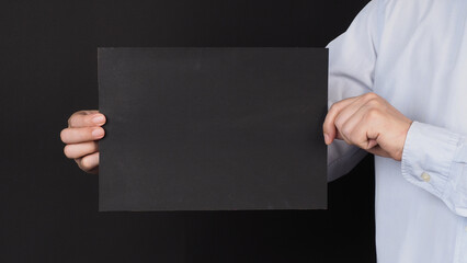 Blank black board A4 paper in man hand covered face and wear blue shirt on black background..