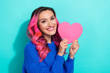 Photo of young cheerful positive hipster lady dyed pink wavy hair wear blue knitted sweater hold paper heart symbol isolated on cyan color background