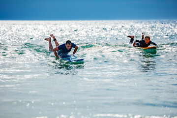 Man and a child paddling in the sea to catch wave on surfboard