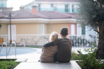 Back view young teens couple, boy and girl sitting hugging outdoor, first dating, flower and kids love.