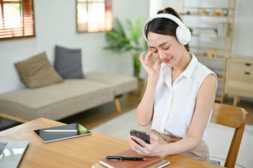 Beautiful Asian woman listening to music though her headphones, selecting a playlist on her phone