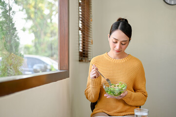 Relaxed Asian woman eating salad vegetables mix at the cafe on the weekend morning.