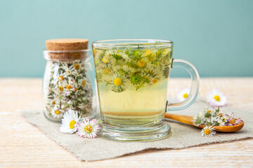 Dried herbal medicinal plant Common Daisy, also known as Bellis Perennis. Dry flower blossoms in glass jar and and herbal tea in glass, indoors still life.