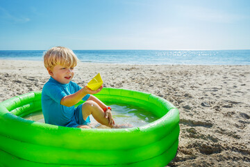 Play in inflatable pool at the beach holding plastic toy ship