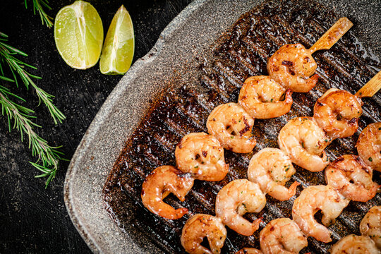 Grilled shrimp on skewers in a frying pan with rosemary and pieces of lime. 