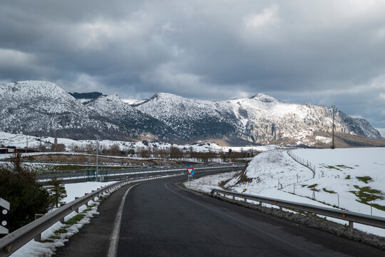 Estrada com uma curva de acesso à autoestrada num dia frio de inverno com muita neve e com montanhas ao fundo também cobertas de neve em Espanha