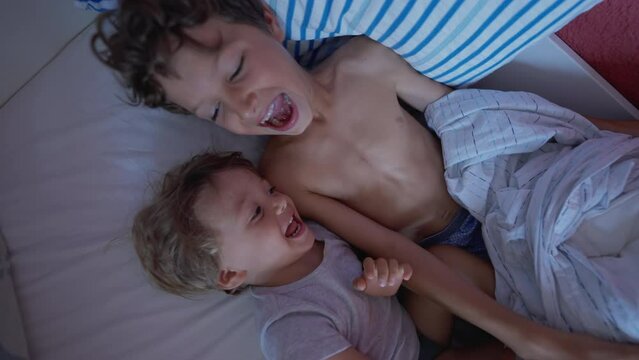Two happy children in bed laughing and smiling. Small siblings having fun together under sheets covering with duvet. Joyful brothers