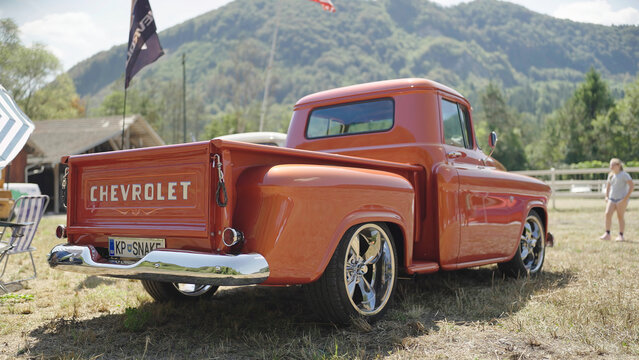 Restored luxury orange retro Chevrolet pickup truck from rear at countryside